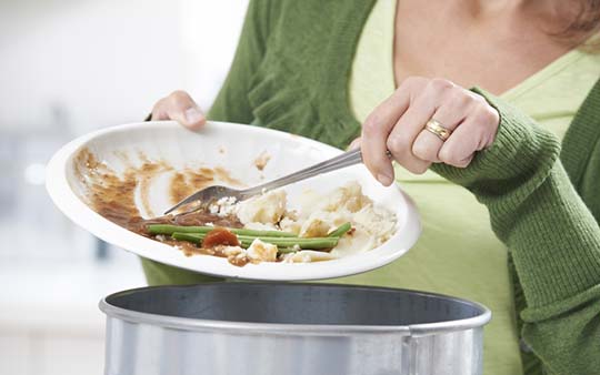 Woman Scraping Uneaten Food off Plate into Garbage Can